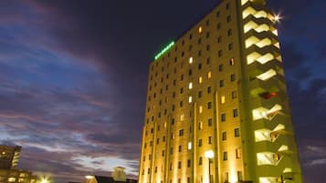 Um hotel de vários andares com um padrão em zigue-zague característico na fachada, janelas iluminadas e uma placa verde no topo.