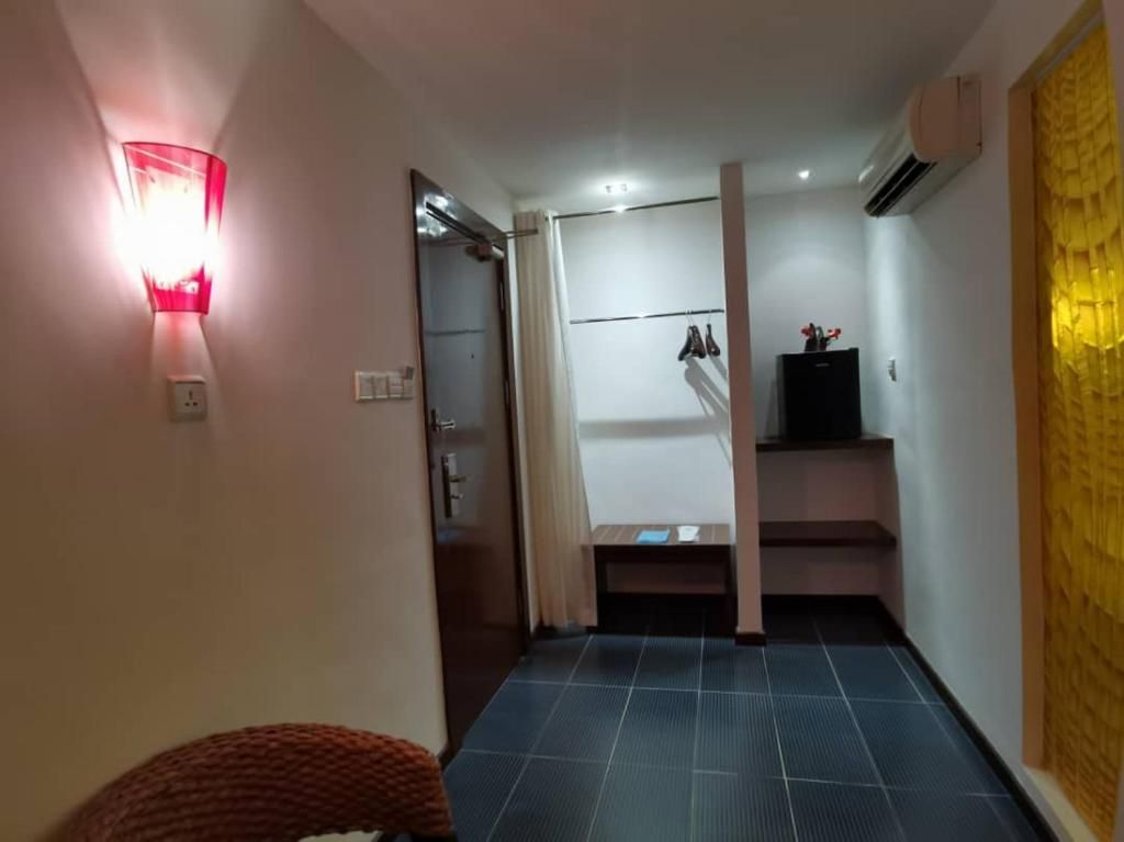 A hotel room with a tiled floor, a bed, a nightstand, a wall-mounted lamp, and a window with curtains.