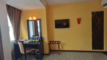 A hotel room with a bed, a desk with a chair, a television, and a window with curtains.