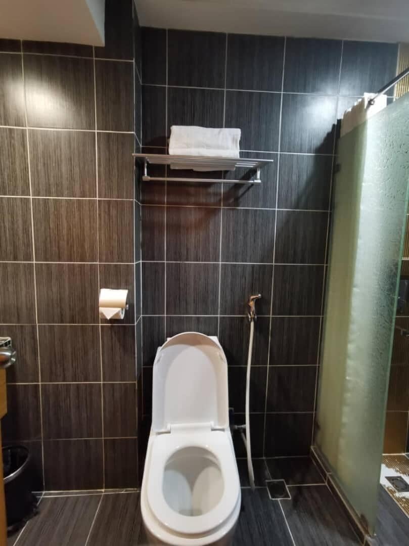 Une salle de bain moderne avec des carreaux de couleur sombre, des toilettes blanches, une douche et un porte-serviettes.