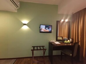 Habitación de hotel con televisor montado en la pared, un escritorio con silla, una mesita y una ventana con cortinas.