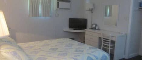 Een hotelkamer met een bed, een bureau met een televisie, een stoel en een kledingkast.