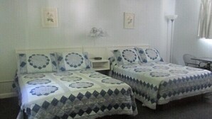 A room with two beds, each with patterned bedding, a small table, and a chair. - Country Squire Motel (Littleton)