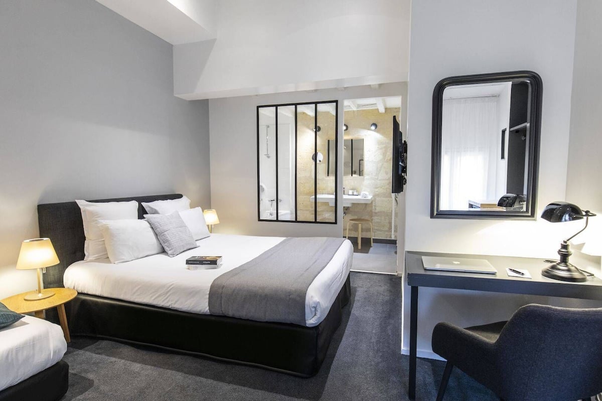Une chambre d’hôtel moderne, dotée d’un grand lit, de tables de chevet avec des lampes, d’un bureau avec une chaise et d’un miroir.