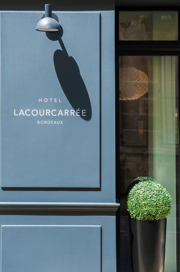 A sign for Hotel Lacourcarrée in Bordeaux, featuring a modern lamp and a potted plant.