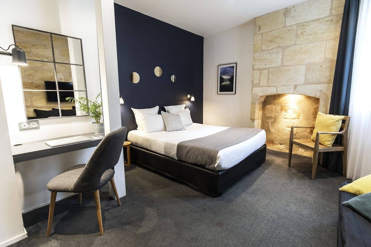 Une chambre moderne avec un lit, un bureau, une chaise et un mur en pierre.