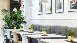 Un comedor moderno con asientos tapizados en gris, mesas blancas y macetas doradas.