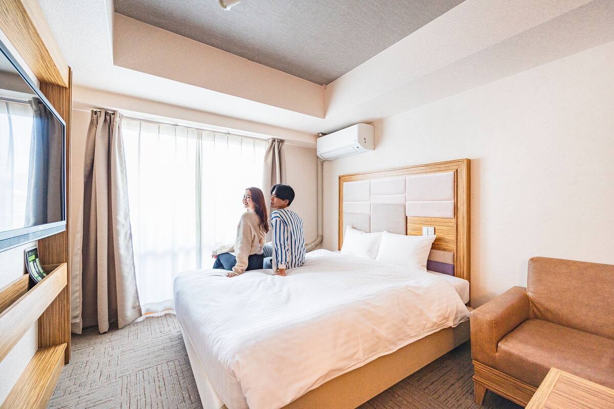A hotel room with a large bed, a TV, a wooden headboard, and a brown leather armchair.