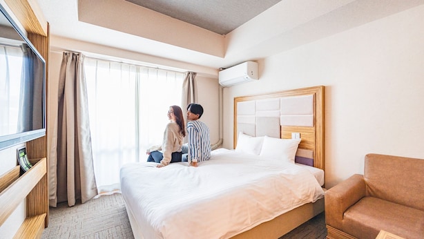 A hotel room with a large bed, a TV, a wooden headboard, and a brown leather armchair. - Hotel Relief Namba Daikokuchou (Osaka)