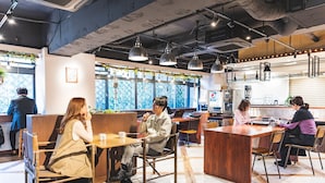 A modern cafe with wooden tables and chairs, large windows with a view, and hanging pendant lights. - Hotel Relief Namba Daikokuchou (Osaka)