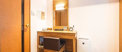 A hotel room with a wooden desk, a large mirror, a small heater, and a trash bin.