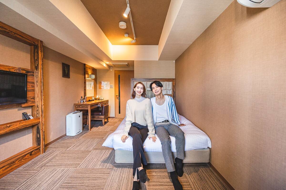 A hotel room with a bed, a desk, a television, and a wall-mounted air conditioner.