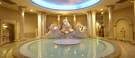 A grand lobby with a central fountain, columns, and classical statues.