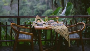 A wooden deck with two wicker chairs, a table set with plates, glasses, and a woven light fixture. - Adiwana Svarga Loka (Ubud)