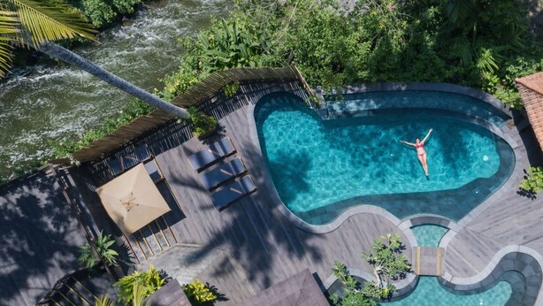 An aerial view of a swimming pool with a heart-shaped design, surrounded by lush greenery and a river. - Adiwana Svarga Loka (Ubud)