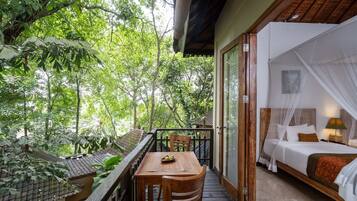 A room with a bed, a table, and a view of the surrounding greenery.