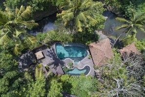 Vista aérea de un complejo turístico con piscina, rodeado de abundante vegetación y palmeras.