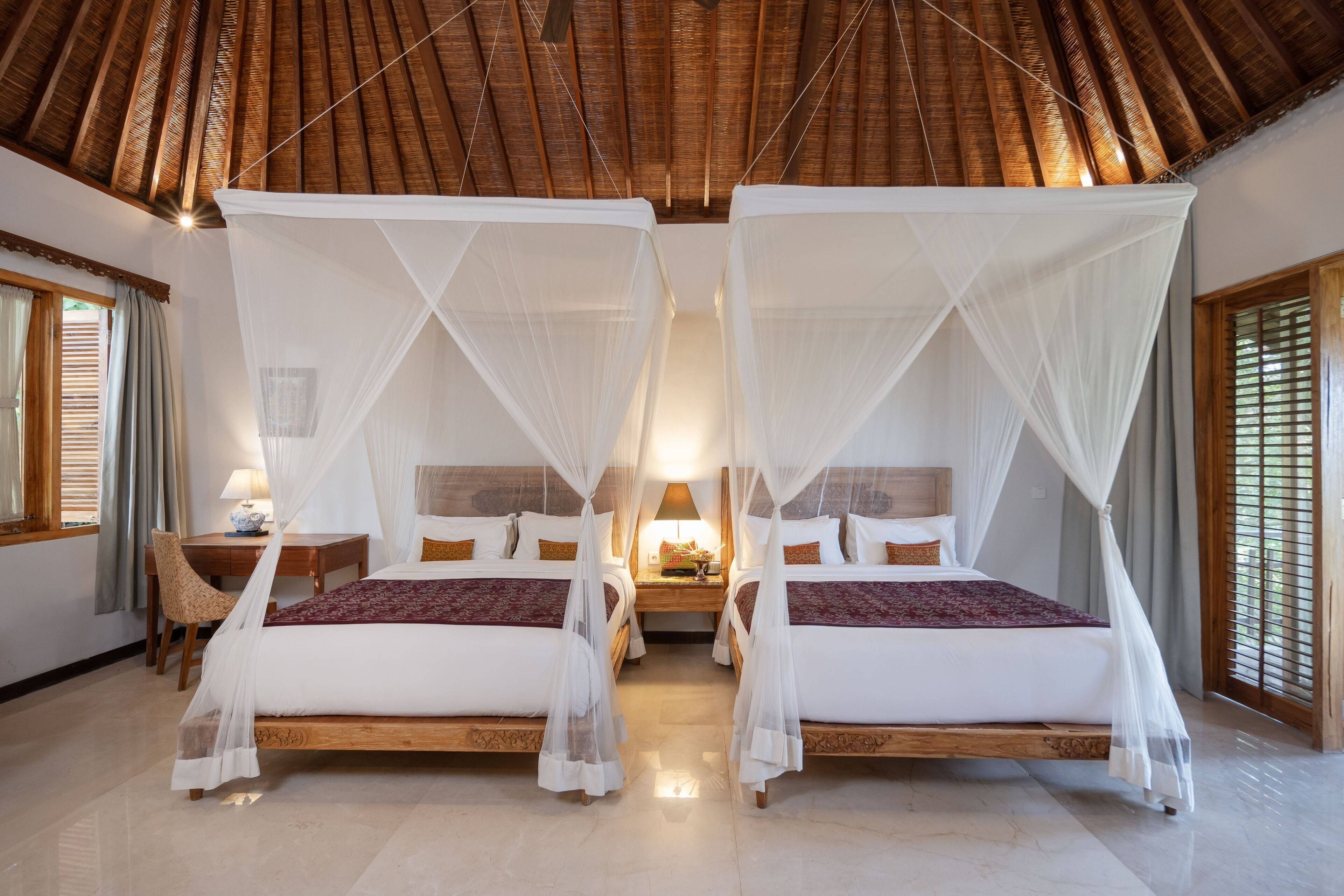 A room with two beds, each with a canopy, a wooden headboard, and a nightstand with a lamp.