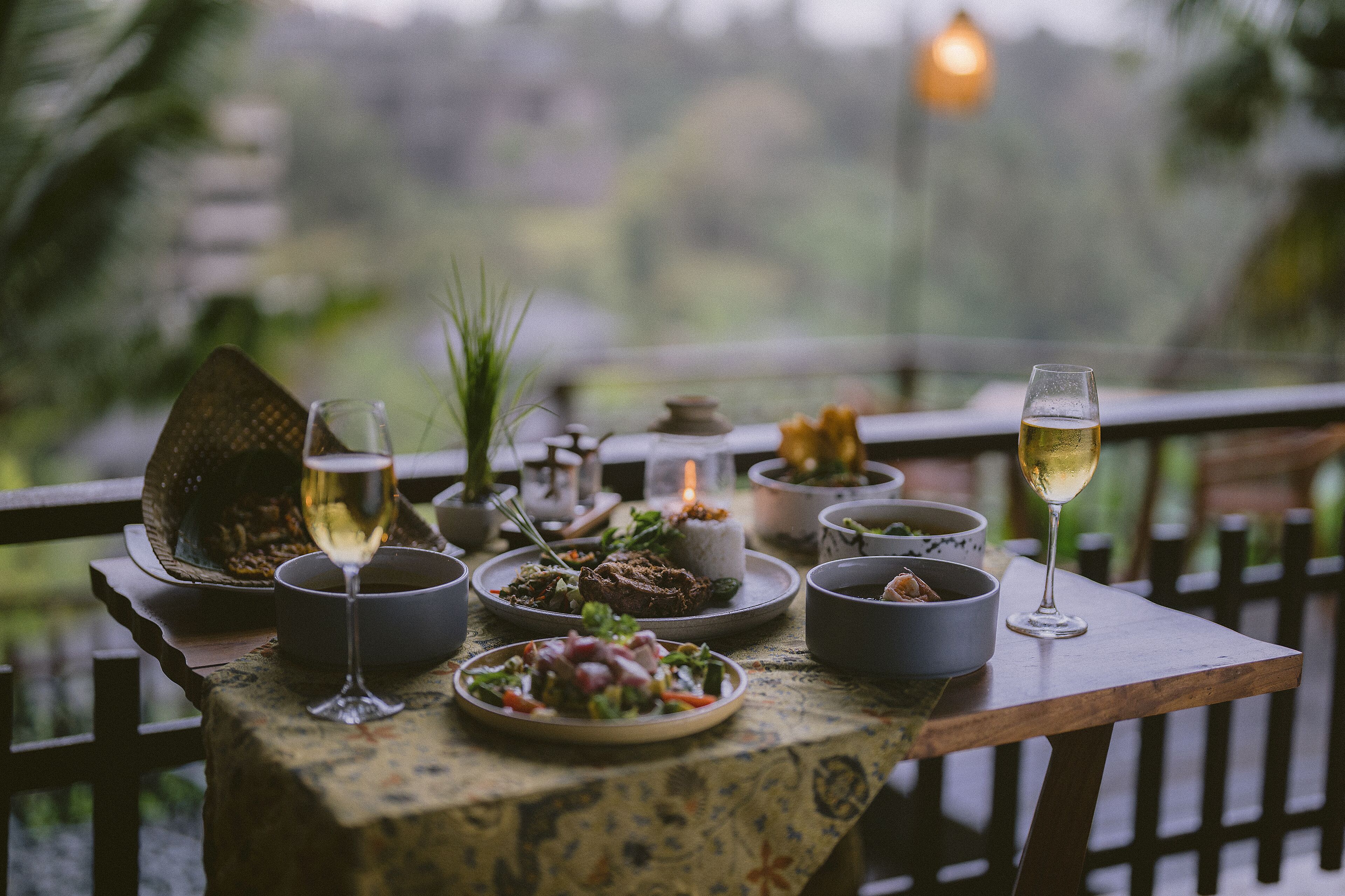 A dining table with various dishes and glasses, set outdoors with a view of greenery.