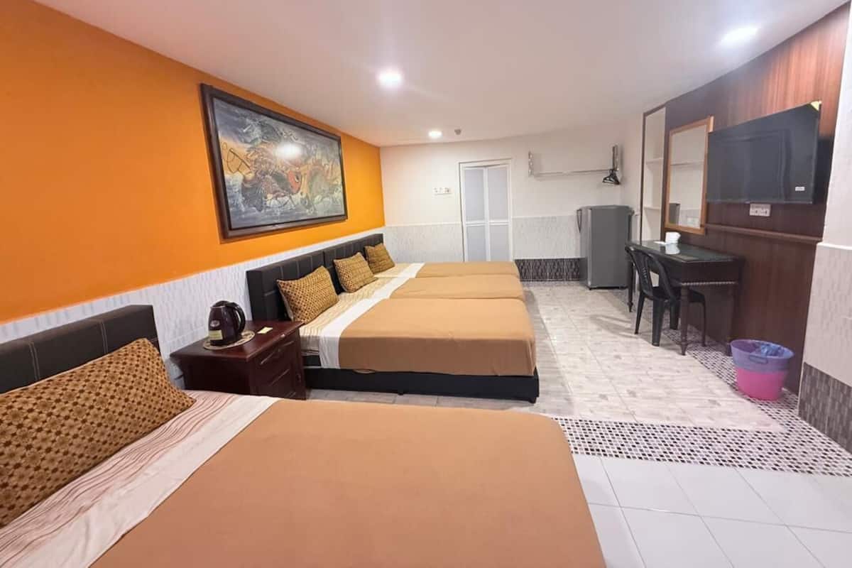 Habitación de hotel con tres camas, un escritorio, una silla, un televisor y un cuadro en la pared.