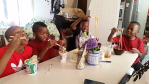 A group of people sitting at a table with food and drinks, a laptop, and a vase with flowers. - Tokyo Guest House 2020 (Tokyo)