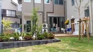 A residential building with a balcony, air conditioning units, and a garden with various plants and flowers. - Tokyo Guest House 2020 (Tokyo)