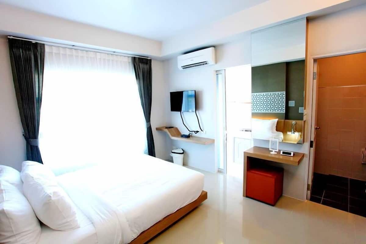 A modern hotel room with a large bed, a TV, a small desk, and a bathroom with a mirror and sink.