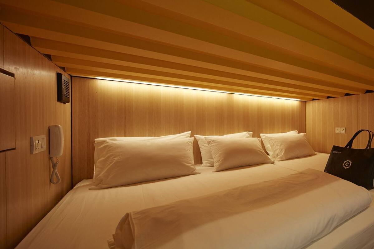 A hotel room with a wooden ceiling, a bed with white bedding, a black handbag on the bed, and a red door.