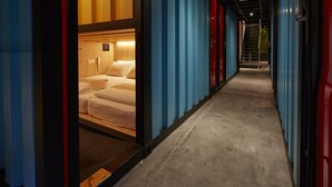 Un pasillo de hotel con una cama en una habitación, paredes azules y rojas, y suelo de hormigón.