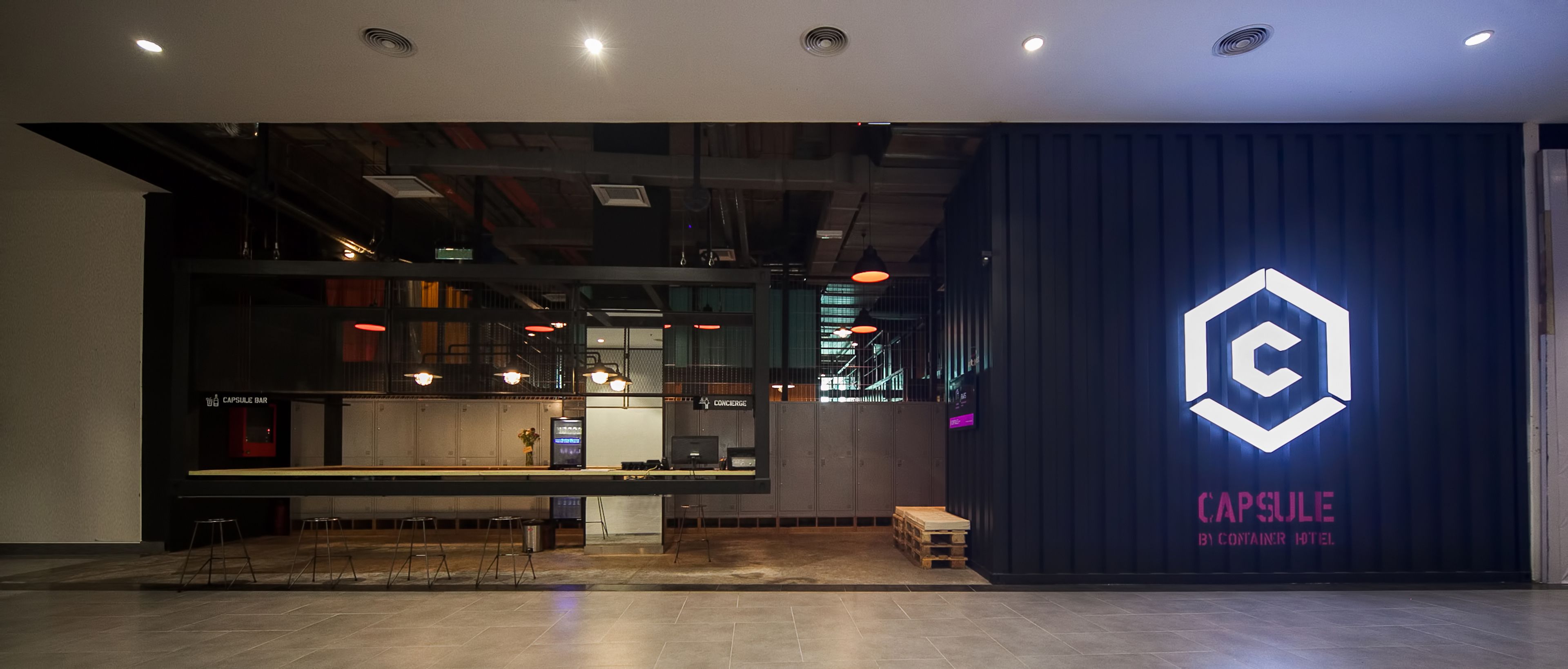 A modern hotel lobby with a bar area, a reception desk, and a logo on the wall.