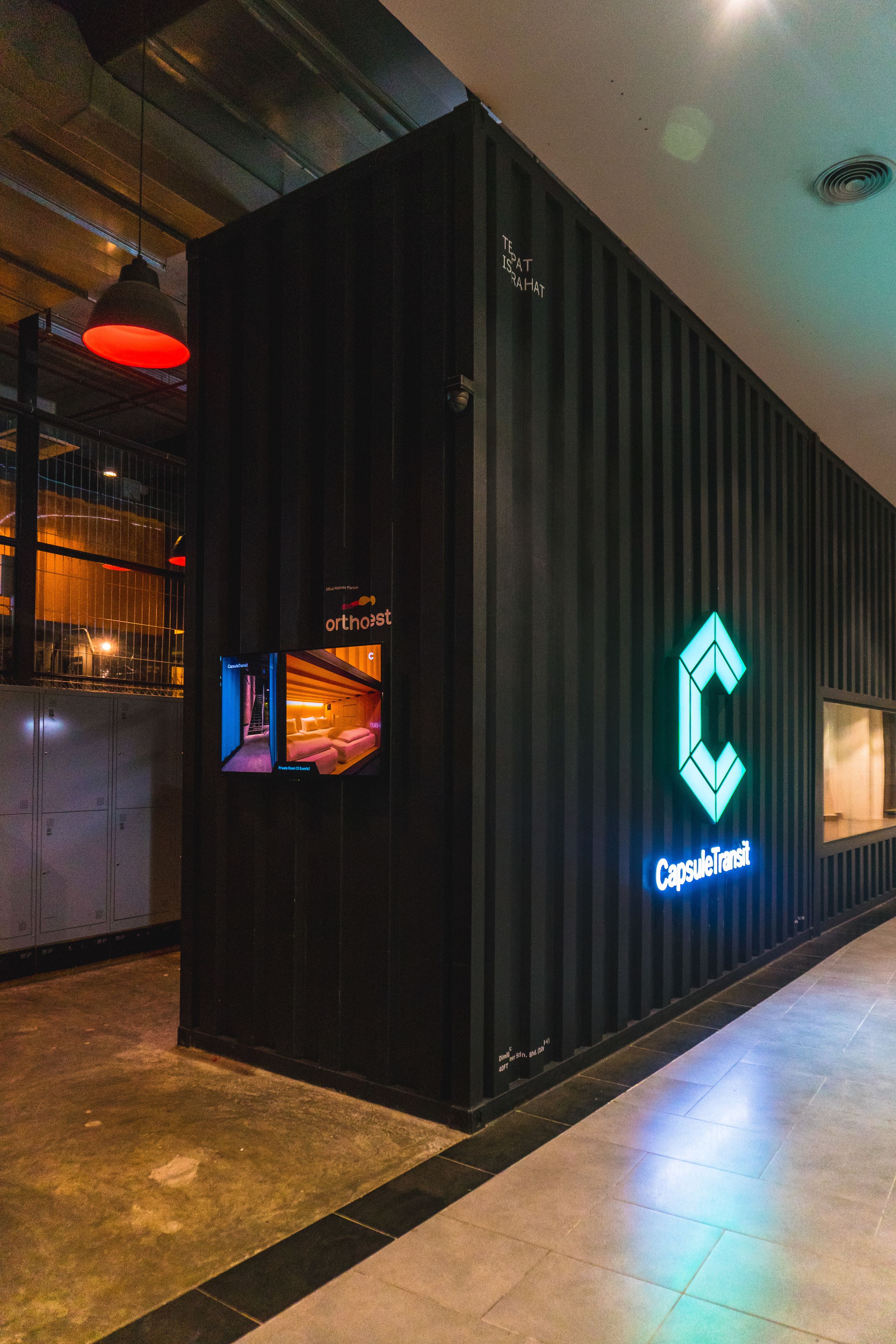 A CapsuleTransit branded hotel with a modern design, featuring a large illuminated logo and a view into the interior.