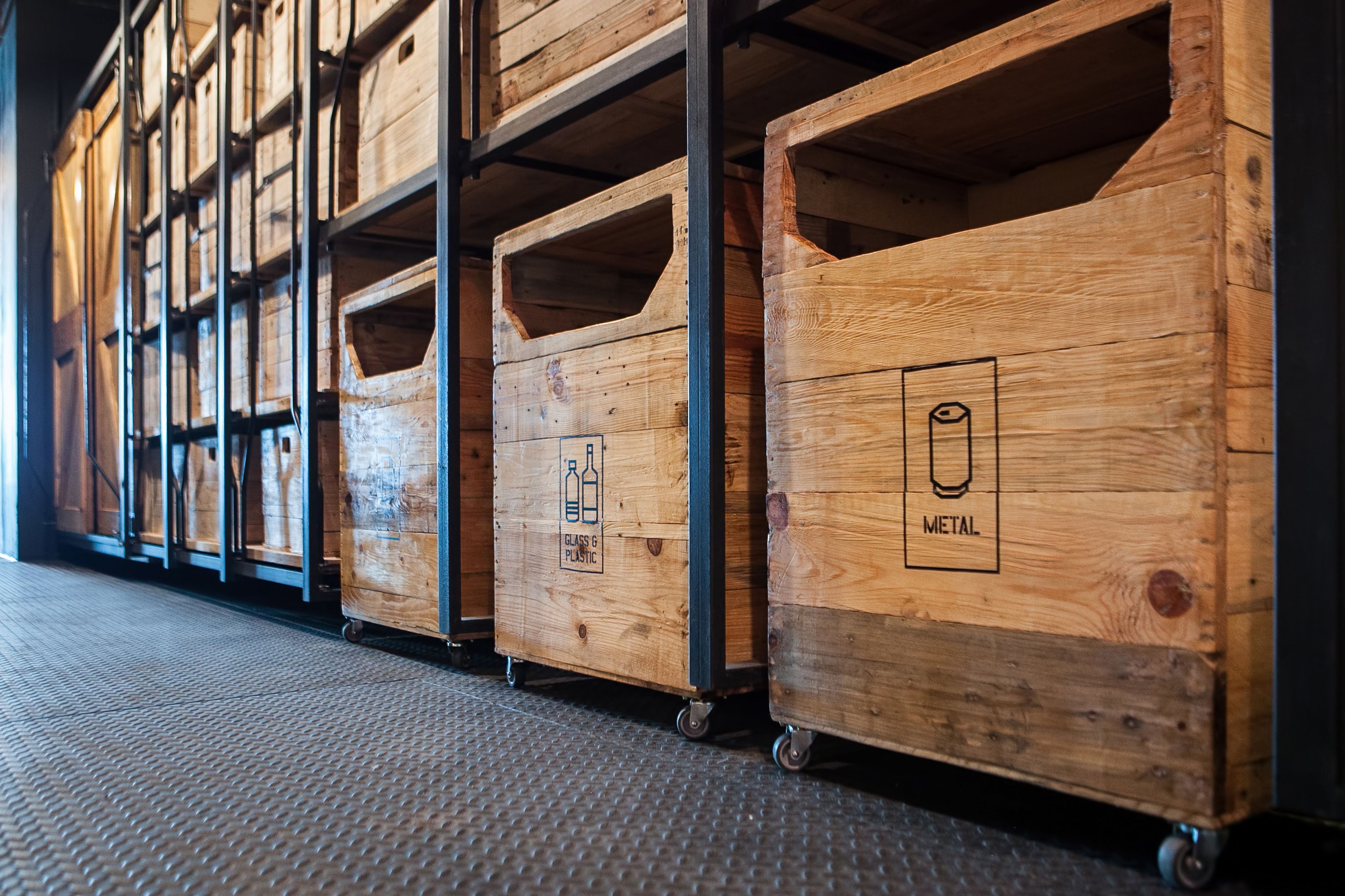 Wooden storage bins with wheels, some labeled "Glass & Plastic" and "Metal."