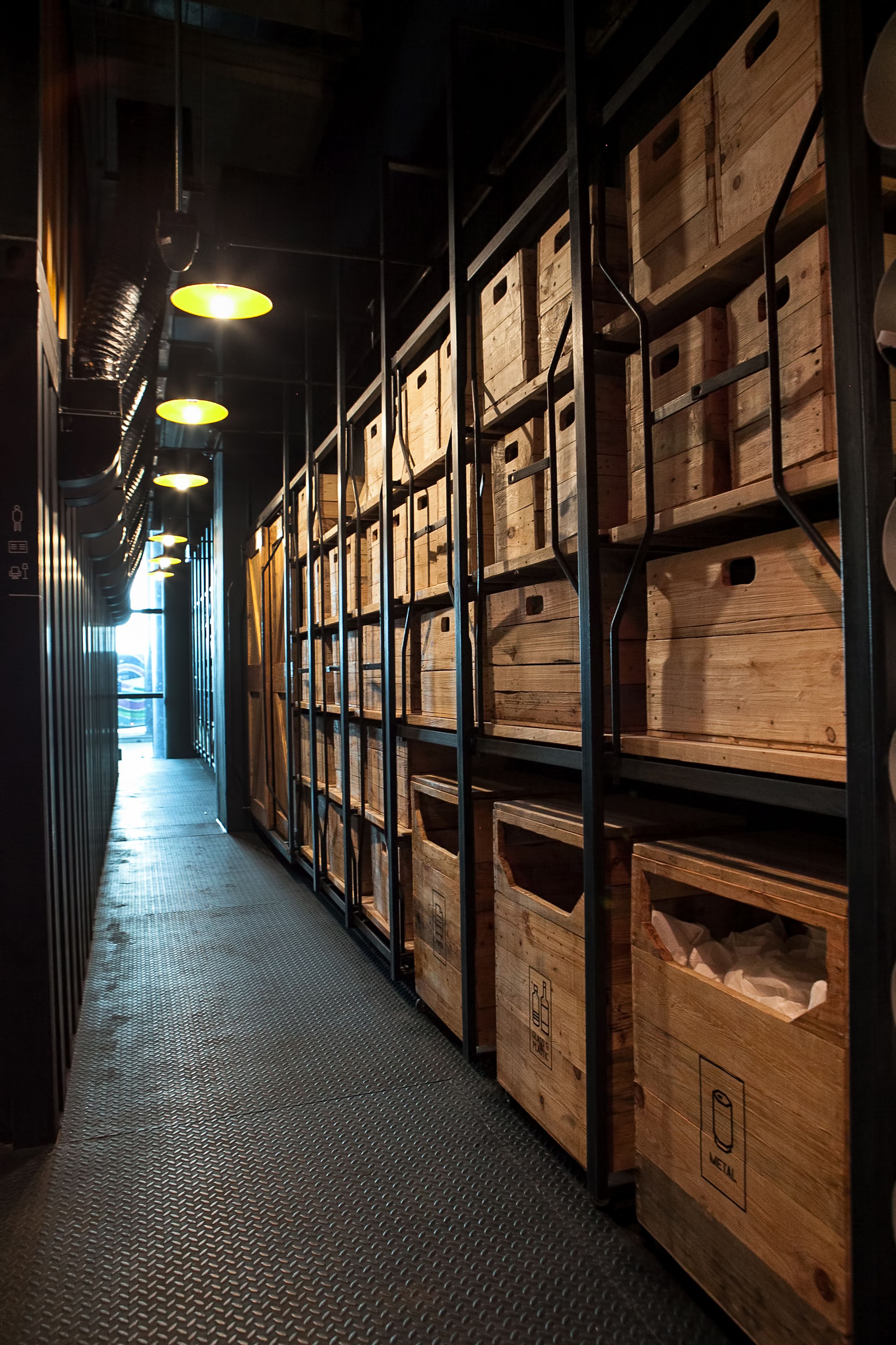 A narrow hallway with wooden crates on shelves and hanging lights.
