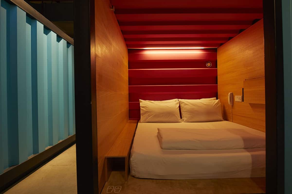 A compact, modern bedroom with a wooden bed, a red ceiling, and a blue wall.