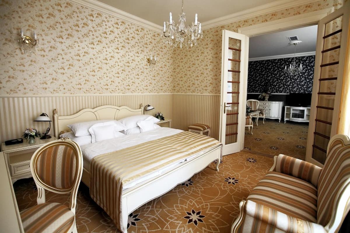 A bedroom with a bed, two chairs, a desk, and a chandelier.
