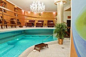 An indoor swimming pool with a wooden bench and a pool table, surrounded by seating and a chandelier. - GOLDEN ROYAL Boutique hotel & Spa (Kosice)