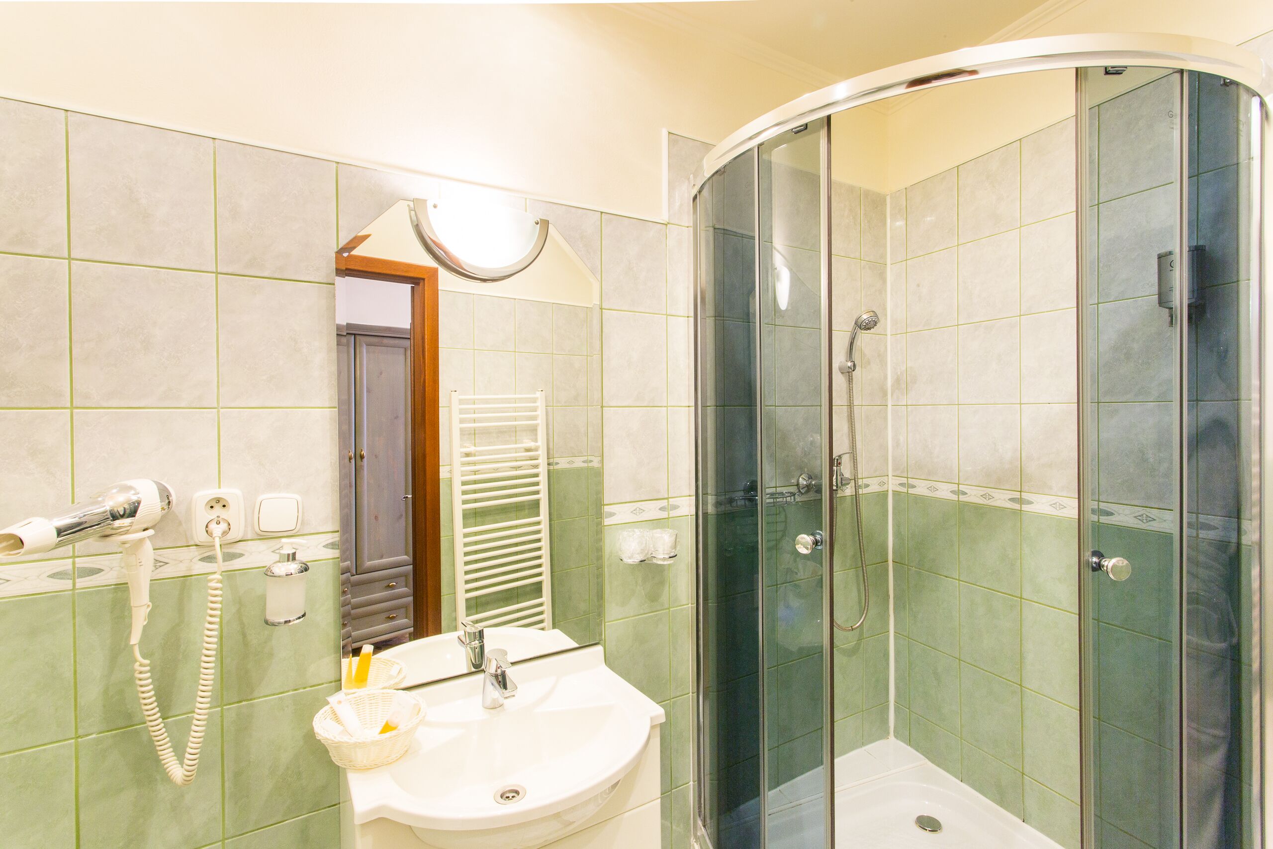 Un baño con cabina de ducha curvada, lavabo con espejo y secador de pelo en la pared.