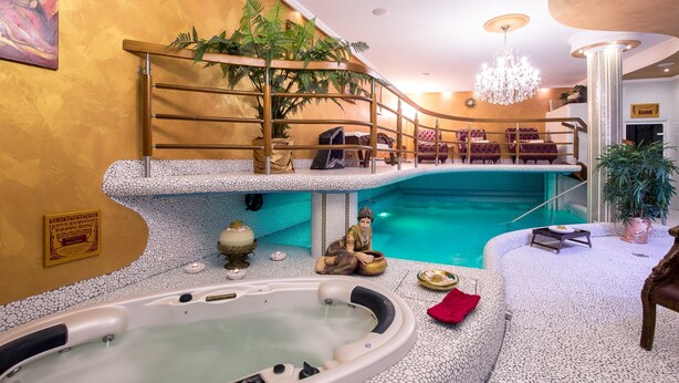 Un área de piscina interior lujosa con un jacuzzi, asientos y una escalera que lleva a un balcón.