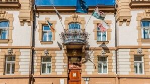 Un edificio histórico con una entrada destacada, banderas y un balcón con barandillas ornamentales.