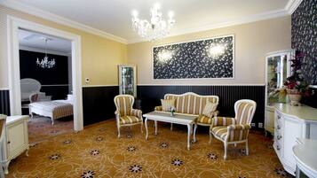Una habitación con alfombra estampada, un candelabro, sillones a rayas, una mesa blanca y una obra de arte floral grande en la pared.