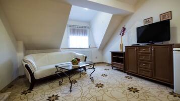 A living room with a white sofa, a glass coffee table with fruit, a TV on a wooden cabinet, and a patterned carpet.