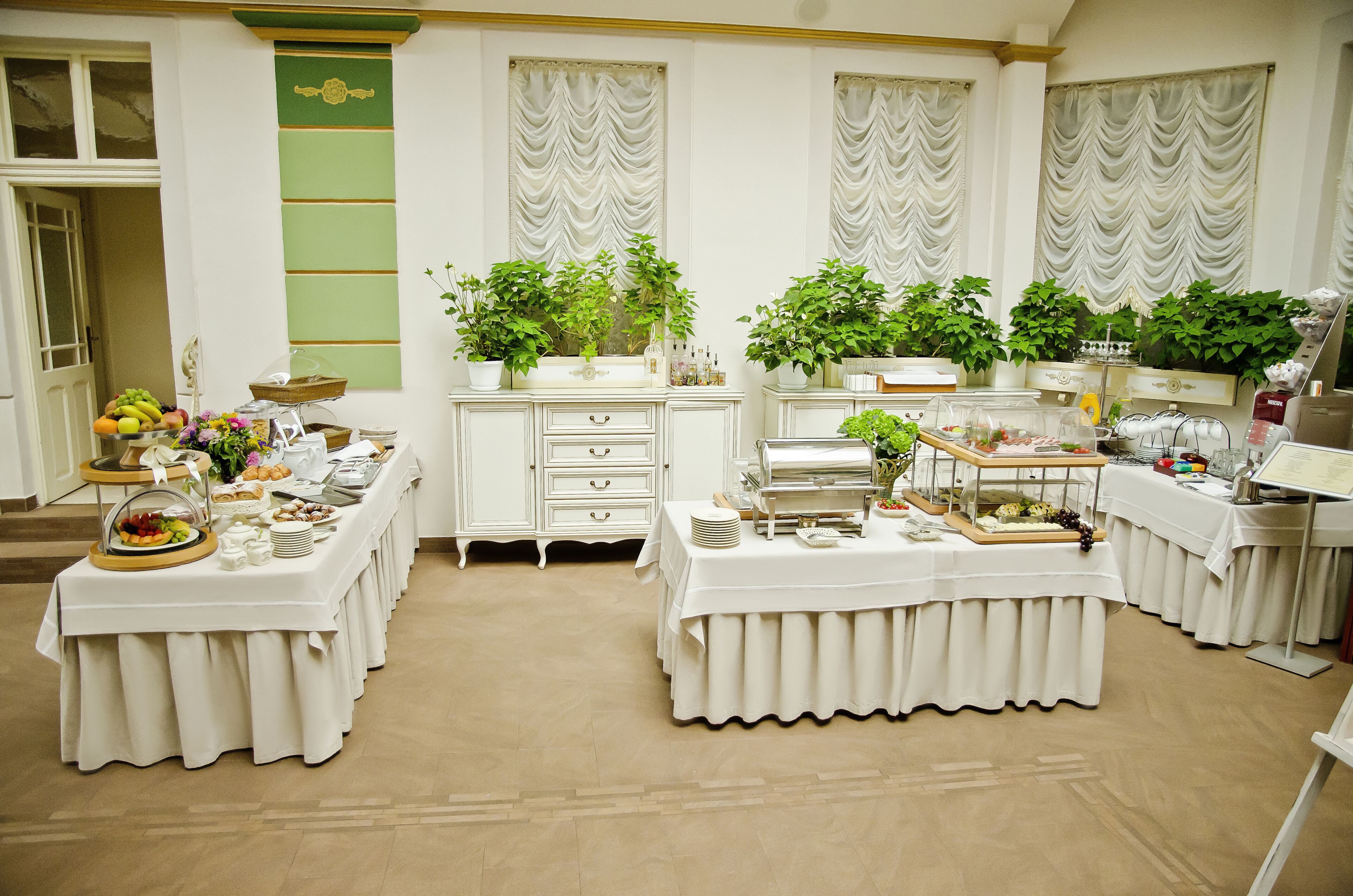 Un salón de banquetes con múltiples mesas dispuestas para un bufé, que incluye diversos alimentos y plantas decorativas.