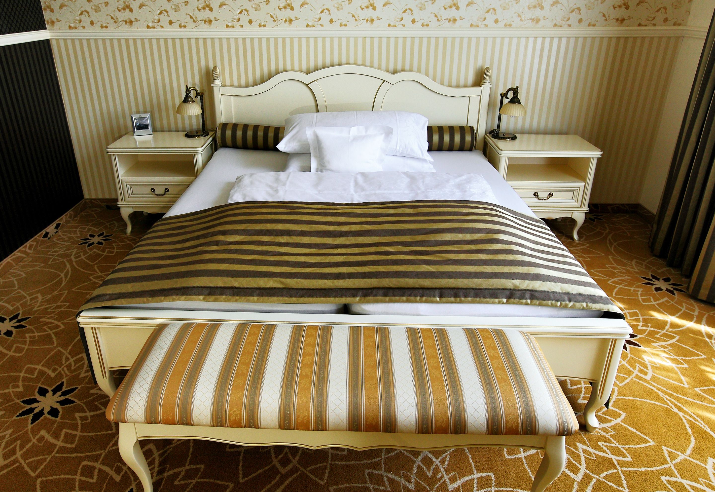 A bed with a striped bedspread, two bedside tables with lamps, and a patterned carpet.