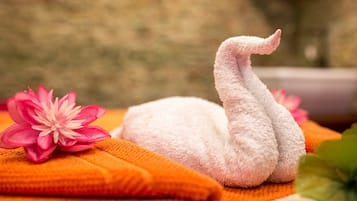 Una toalla con forma de cisne sobre una toalla naranja, con una flor rosa a su lado.