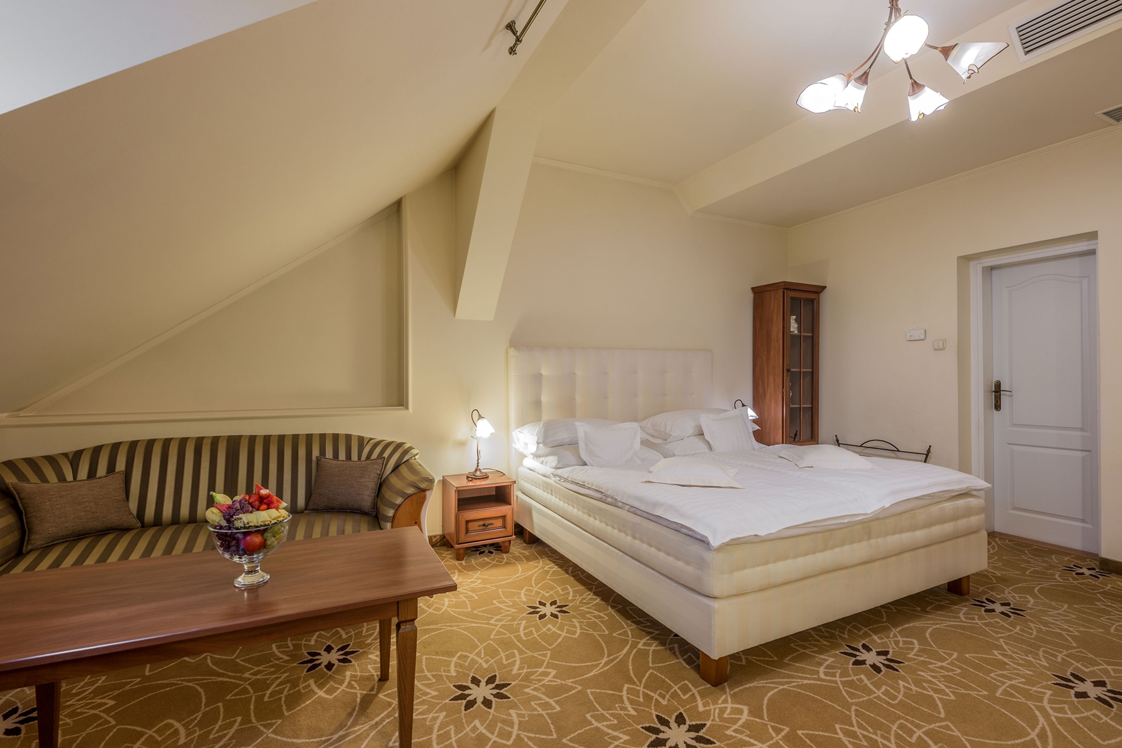 Un dormitorio con cama, mesita de noche, lámpara, armario de madera, sofá y una mesa con frutero.