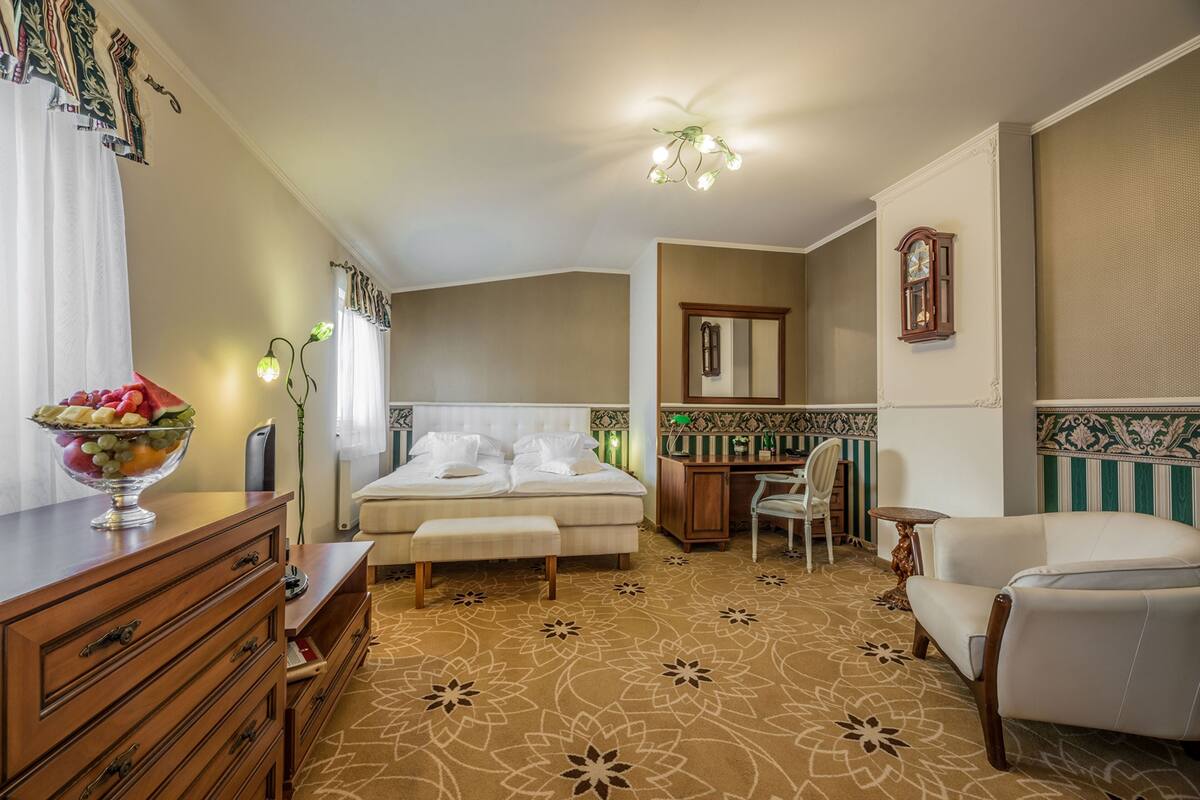 A hotel room with a bed, a desk, a chair, a dresser, and a decorative bowl on the dresser.