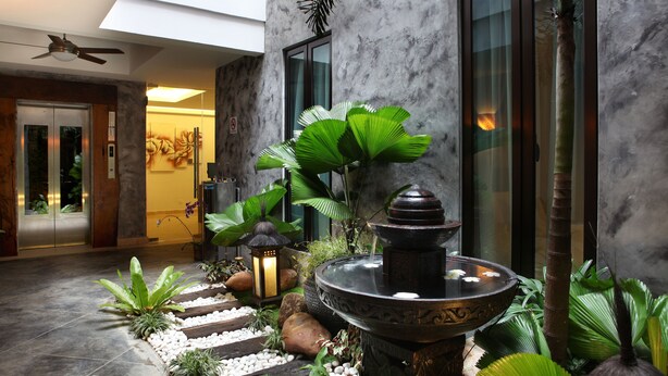 A modern indoor garden with a water feature, stone steps, and lush greenery. - Hotel Richbaliz (Batu Caves)