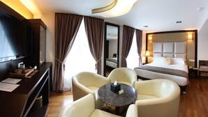 A hotel room with a bed, a desk with a TV, a chair, a table, and a large mirror. - Hotel Richbaliz (Batu Caves)