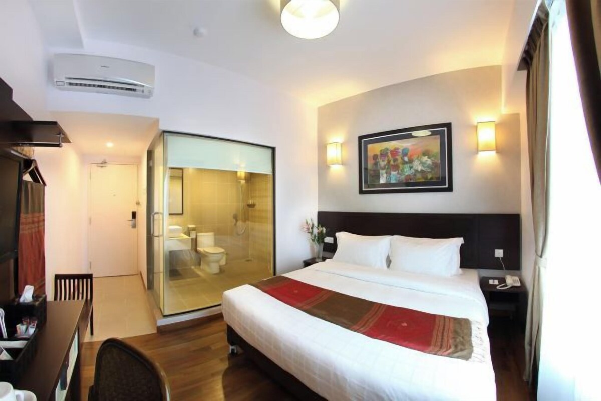 Habitación de hotel con cama, escritorio, silla, cabina de ducha de vidrio y un cuadro en la pared.