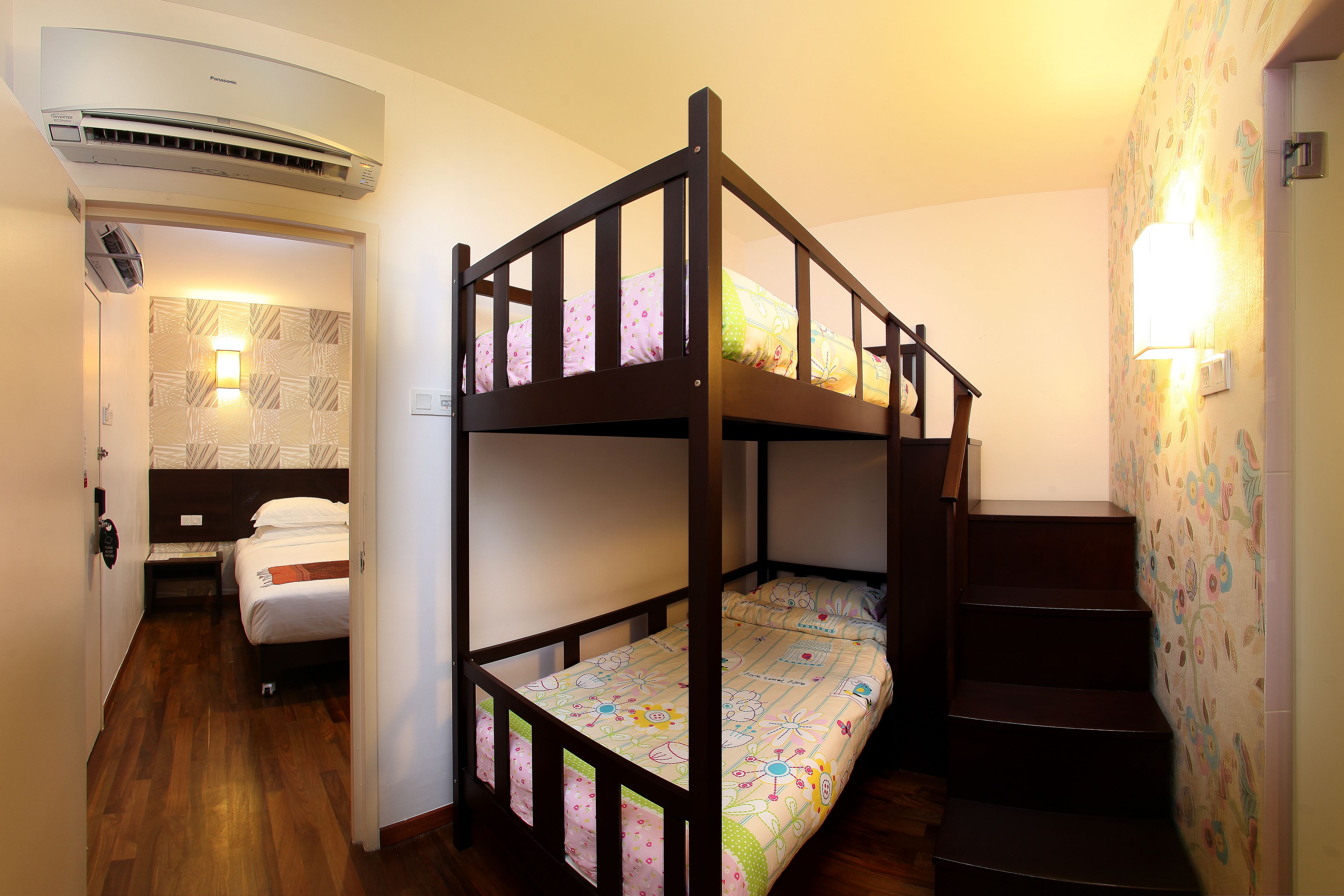 A bunk bed room with a wooden headboard, a staircase, and a wall-mounted light fixture.